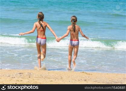 Girls holding hands run into the sea