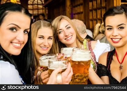 Girls in traditional Dirndl dresses are drinking beer and having fun at the Oktoberfest, mixed races: One Asian, one Russian, two Caucasian girls