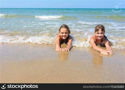 Girls lie on the sand of the sea coast and happily look at the frame