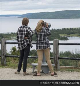 Girls looking at bay view through a coin-operated binoculars, Joey&rsquo;s Lookout, Gambo, Newfoundland And Labrador, Canada