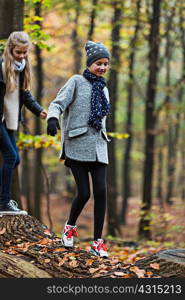 Girls walking on tree trunk in autumn forest