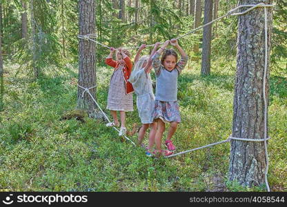 Girls wearing retro clothes balancing on ropes in forest