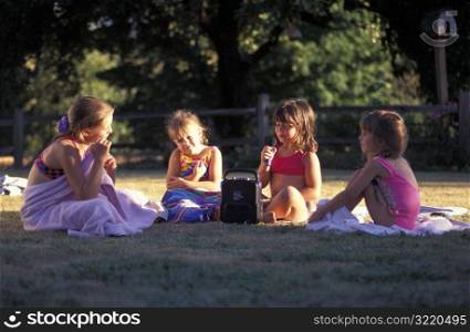 Girls Wearing Swimsuits And Sitting On Towels In Park