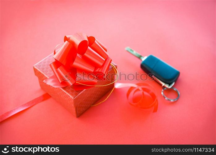 Give gift car key concept / Red gift box with red ribbon bow and key car as present on red background