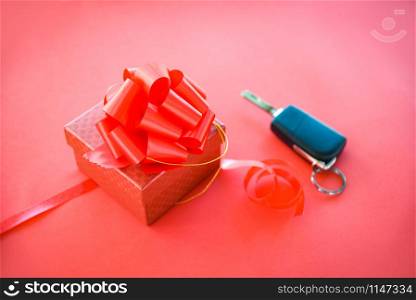 Give gift car key concept / Red gift box with red ribbon bow and key car as present on red background
