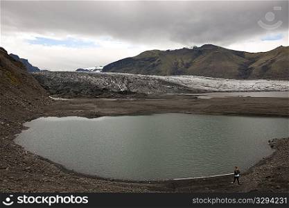 Glacier and glacial lake surrounded by mountains on cloudy day