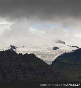 Glacier icecap on jagged mountain, surrounded by clouds
