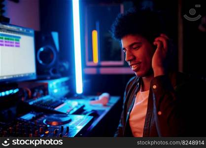 Glad music producer listening new track in headphones working at night in recording studio or radio station. Glad music producer listening new track in headphones