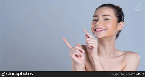 Glamorous beautiful woman with perfect makeup clean skin pointing finger in copyspace isolated background. Promotion indicated by hand gesture concept for skincare product advertisement.. Glamorous woman pointing finger advertising product in isolated background.