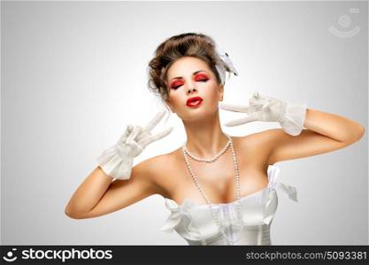 Glamorous gesture.. Sexy pinup bride in a vintage wedding corset showing V sign on grey background.