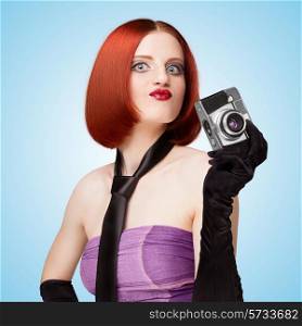 Glamorous girl, retro vamp style, dressed in a necktie and long gloves, showing emotions and holding an old vintage photo camera on blue background.