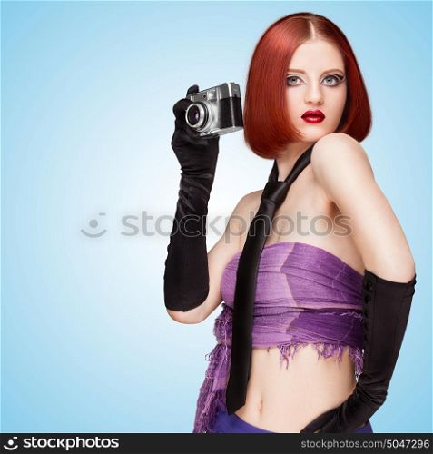 Glamorous girl, vamp style, dressed in a necktie and long gloves, taking a photo with an old vintage photo camera on blue background.