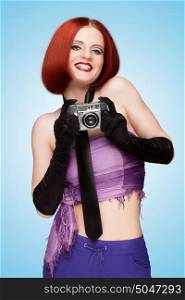 Glamorous happy girl, dressed in a necktie and long gloves, taking a photo with an old vintage photo camera and saying cheese on blue background.
