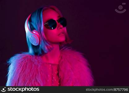 Glamorous hipster teenager in sunglasses and furry coat listening to music with headphones. Portrait of millennial pretty girl with short hairstyle with neon light. Dyed blue and pink hair. Glamorous hipster teenager in sunglasses and furry coat listening to music with headphones. Portrait of millennial pretty girl with short hairstyle with neon light. Dyed blue and pink hair.