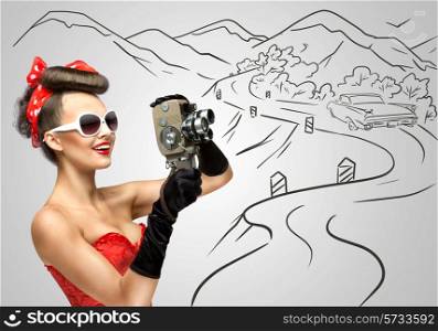 Glamorous pin-up girl filming nature and countryside with an old retro cinema 8 mm camera, standing in front of a road on grey sketchy background.