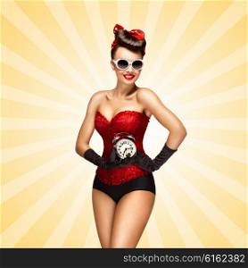 Glamorous pinup girl in a red vintage corset holding a retro alarm clock in her hand and smiling on colorful abstract cartoon style background.