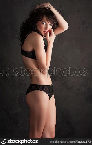 Glamorous sexy standing woman in black lingerie on black background