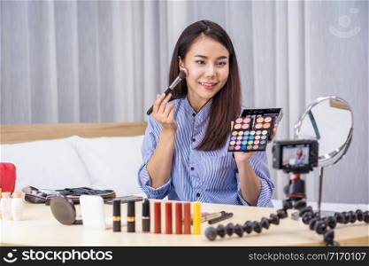 Glamour Asian woman beauty blogger or vlogger showing make up with palette and Live on social network media via video or mobile phone, video recording by herself,makeup tutorial,cosmetics vlog concept