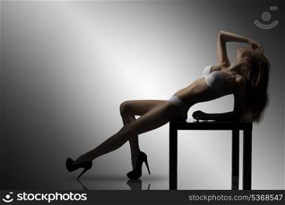 glamour backlight portrait of sexy brunette girl with white lingerie and heels posing on small table