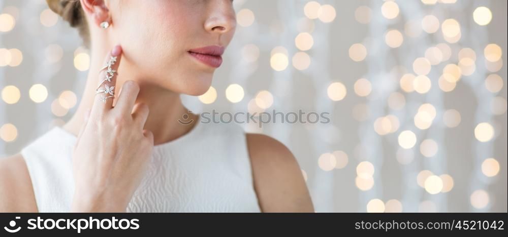 glamour, beauty, jewelry and luxury concept - close up of beautiful woman with golden ring and diamond earring over holidays lights background