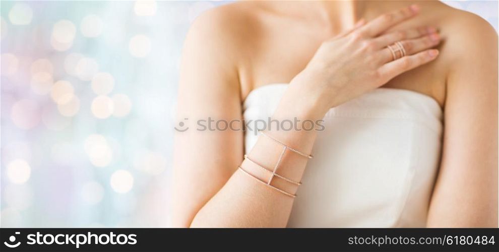 glamour, beauty, jewelry and luxury concept - close up of beautiful woman with golden ring and bracelet over holidays lights background