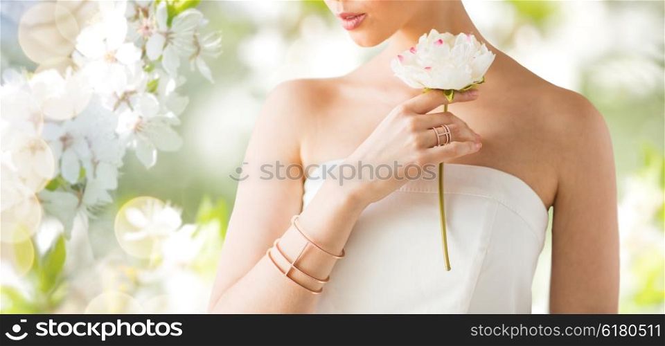 glamour, beauty, jewelry and luxury concept - close up of beautiful woman with golden ring and bracelet holding flower over natural spring cherry blossom