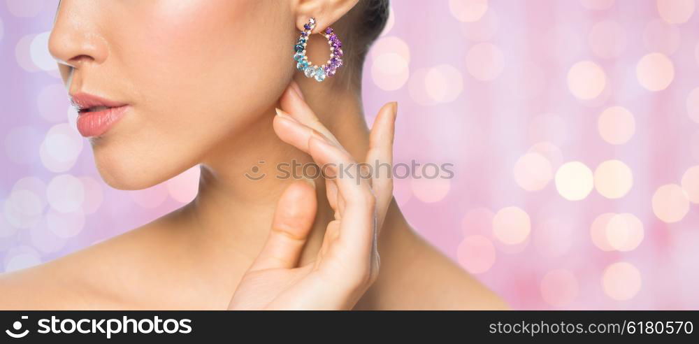 glamour, beauty, jewelry and luxury concept - close up of beautiful woman face with earring over pink holidays lights background