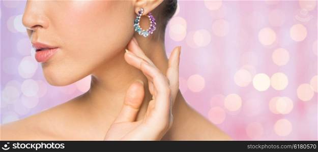 glamour, beauty, jewelry and luxury concept - close up of beautiful woman face with earring over pink holidays lights background