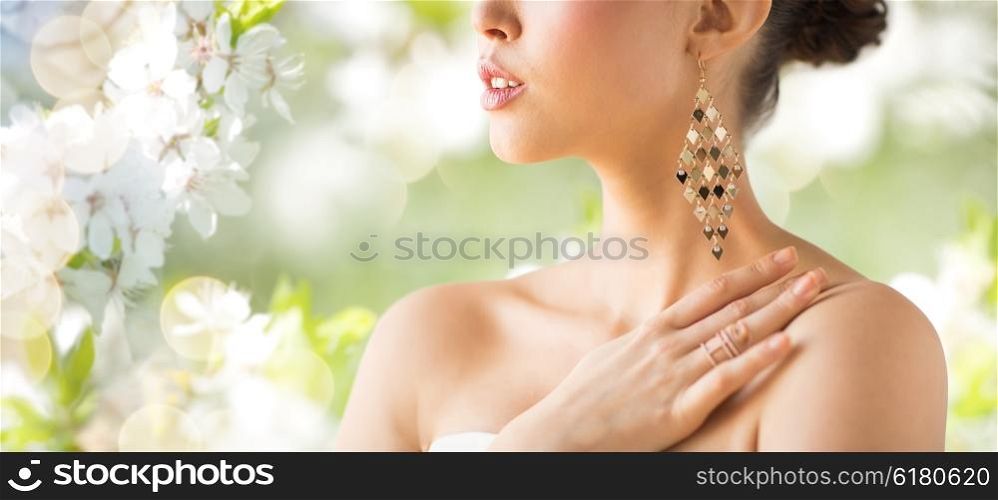 glamour, beauty, jewelry and luxury concept - close up of beautiful woman with earrings over natural spring cherry blossom