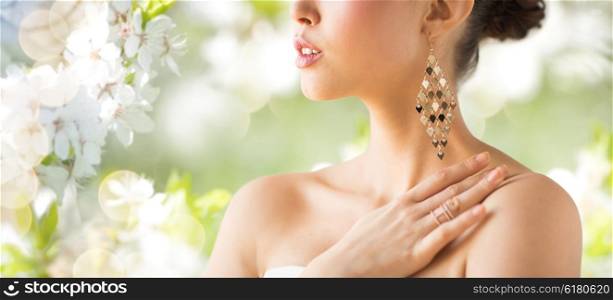 glamour, beauty, jewelry and luxury concept - close up of beautiful woman with earrings over natural spring cherry blossom