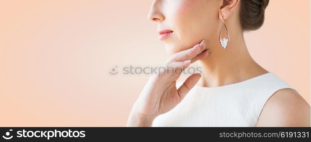 glamour, beauty, jewelry and luxury concept - close up of beautiful woman face with pearl earring over beige background
