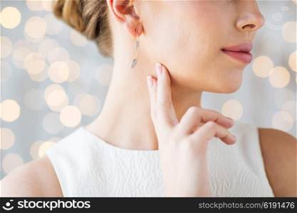 glamour, beauty, jewelry and luxury concept - close up of beautiful woman face with gold and diamond earring over holidays lights background