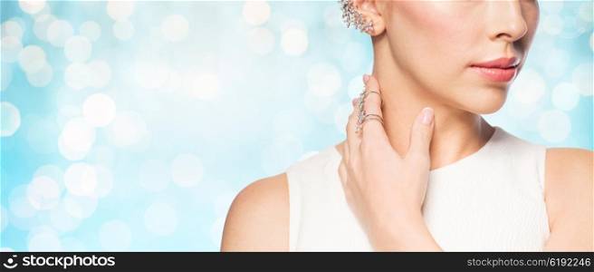 glamour, beauty, jewelry and luxury concept - close up of beautiful woman with golden ring and diamond earring over blue holidays lights background