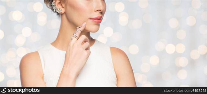 glamour, beauty, jewelry and luxury concept - close up of beautiful woman with golden ring and diamond earring over holidays lights background