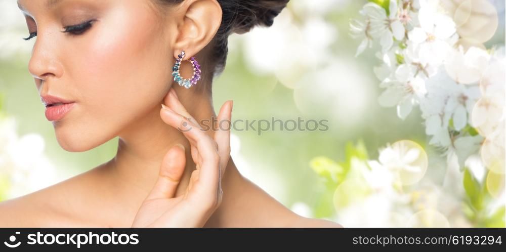 glamour, beauty, jewelry and luxury concept - close up of beautiful woman face with earring over natural spring cherry blossom