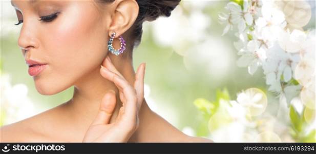 glamour, beauty, jewelry and luxury concept - close up of beautiful woman face with earring over natural spring cherry blossom