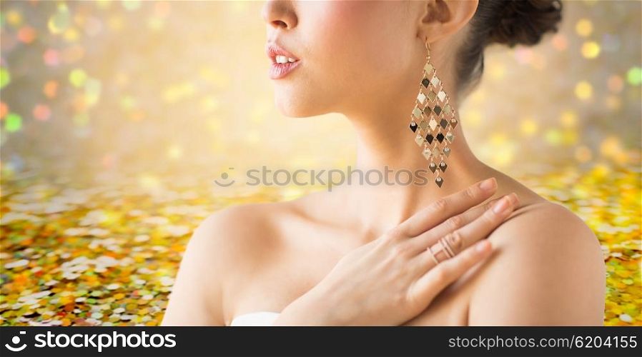 glamour, beauty, jewelry and luxury concept - close up of beautiful woman with earrings over golden holidays lights background