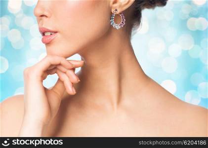 glamour, beauty, jewelry and luxury concept - close up of beautiful woman face with earring over blue holidays lights background