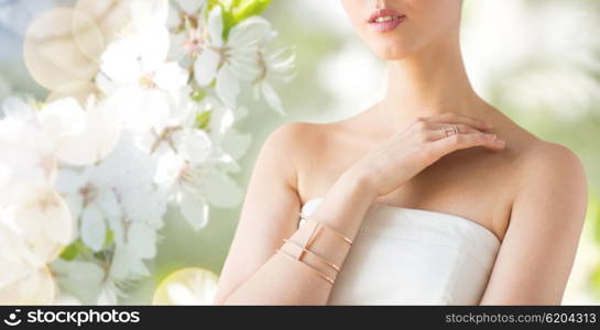 glamour, beauty, jewelry and luxury concept - close up of beautiful woman with golden ring and bracelet over natural spring cherry blossom