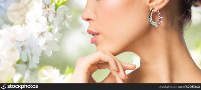 glamour, beauty, jewelry and luxury concept - close up of beautiful woman face with earring over natural spring cherry blossom