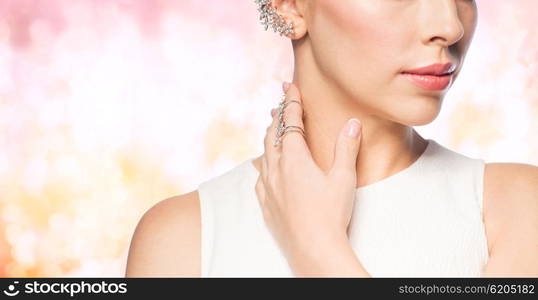 glamour, beauty, jewelry and luxury concept - close up of beautiful woman with golden ring and diamond earring over pink holidays lights background