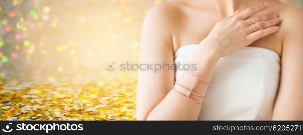 glamour, beauty, jewelry and luxury concept - close up of beautiful woman with golden ring and bracelet over golden holidays lights background