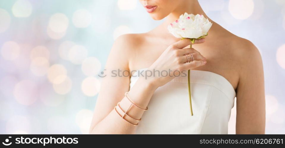 glamour, beauty, jewelry and luxury concept - close up of beautiful woman with golden ring and bracelet holding flower over holidays lights background