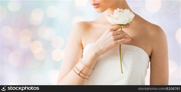 glamour, beauty, jewelry and luxury concept - close up of beautiful woman with golden ring and bracelet holding flower over holidays lights background