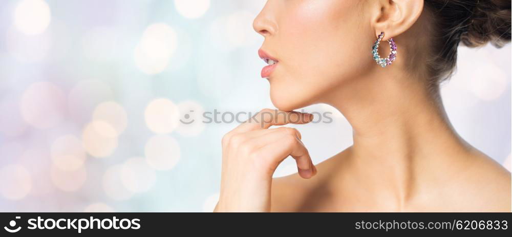 glamour, beauty, jewelry and luxury concept - close up of beautiful woman face with earring over holidays lights background