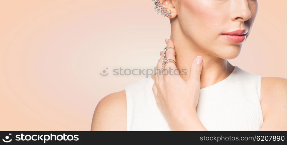 glamour, beauty, jewelry and luxury concept - close up of beautiful woman with golden ring and diamond earring over beige background