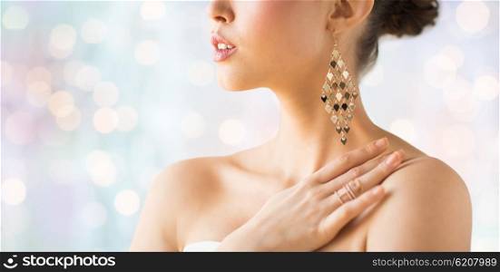 glamour, beauty, jewelry and luxury concept - close up of beautiful woman with earrings over holidays lights background