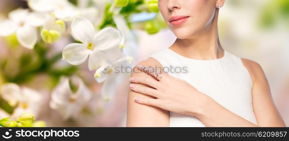 glamour, beauty, jewelry and luxury concept - close up of beautiful woman with golden ring and diamond earring over natural spring lilac blossom background