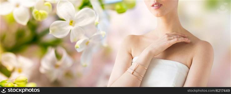 glamour, beauty, jewelry and luxury concept - close up of beautiful woman with golden ring and bracelet over natural spring lilac blossom background