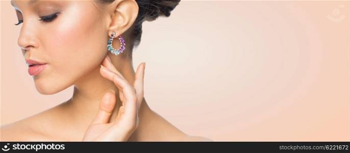 glamour, beauty, jewelry and luxury concept - close up of beautiful woman face with earring over beige background